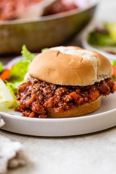 a sloppy joe sandwich on a plate with lettuce and carrots next to it