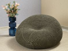 a knitted bean bag sits on the floor next to a blue vase with flowers