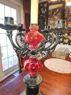 a red glass candle holder sitting on top of a table next to a wooden table