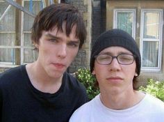 two young men standing next to each other in front of a brick building with windows