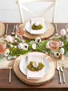 the table is set for easter dinner with pink and white flowers, moss and eggs