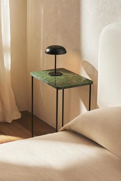 a green table sitting on top of a bed next to a white wall and window