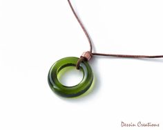 a green necklace with a circular pendant hanging from it's side on a brown cord