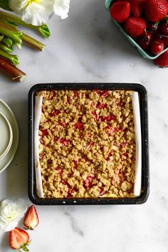 a pan filled with strawberry crisp on top of a counter next to some flowers and strawberries