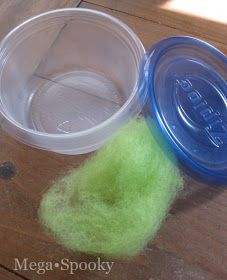 two plastic containers with green wool next to each other on a wooden table, one has a blue lid and the other is clear