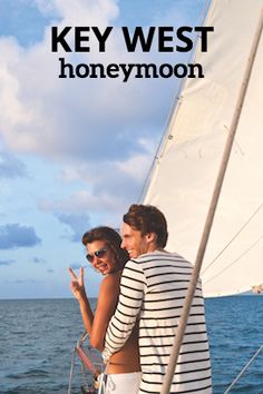 two people standing on the deck of a sailboat, one pointing at the camera