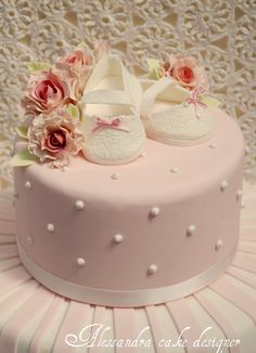 a pink cake decorated with baby shoes and flowers