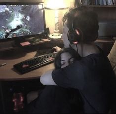 a man and woman sitting in front of a computer monitor with headphones on their ears