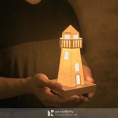 a person holding a paper model of a light house in their hands with the lights on