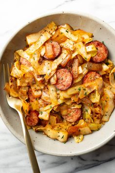 a white bowl filled with potatoes and sausages on top of a marble countertop