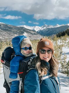 a woman and her child are standing in the snow with mountains in the back ground