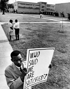 a man holding a sign that says who said we are sattified? on the sidewalk