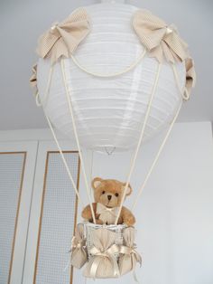 a teddy bear sitting in a basket suspended from the ceiling with ribbon on it's sides