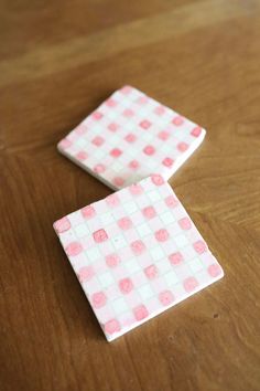 two pink and white checkered coasters sitting on top of a wooden table next to each other