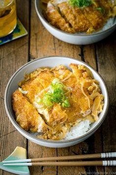 two bowls filled with food and chopsticks on top of a wooden table next to each other