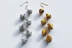 three pairs of gold and silver seashells hanging from hooks on a white surface