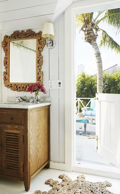 a bathroom with a sink, mirror and door leading to an outside deck area that has a palm tree in the corner