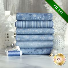 a stack of blue fabric with snowflakes on them and a christmas tree in the background