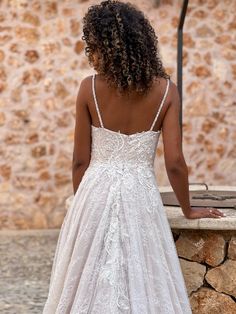 the back of a woman's wedding dress as she stands on a stone wall