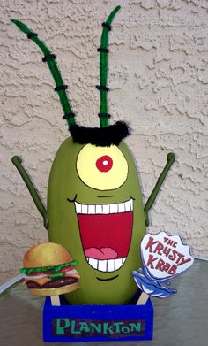 a giant green monster holding a burger and standing in front of a sign that says plankton