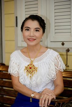 a woman sitting on top of a wooden bench wearing a white shirt and gold necklace