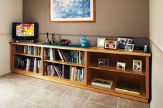 a television sitting on top of a wooden book shelf next to a wall filled with books