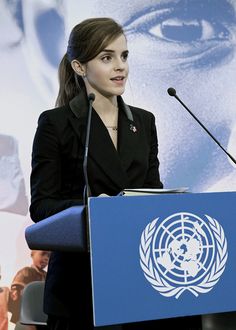 a woman standing at a podium in front of a microphone with an un flag behind her