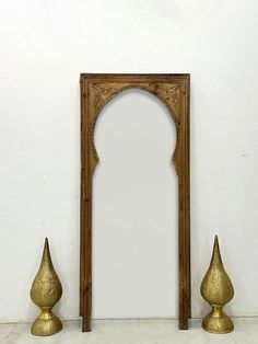 a mirror and two gold vases on a white surface with a wall in the background