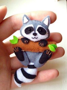 a hand holding a small stuffed raccoon with leaves on it's back