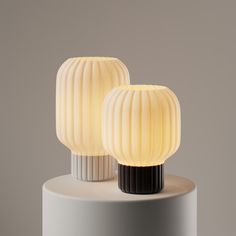 two white and black lamps sitting on top of a gray table next to each other