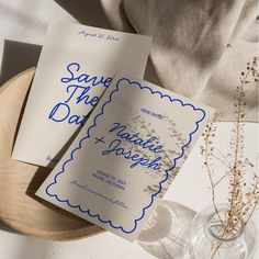 two wedding cards sitting on top of a table next to a vase with dried flowers