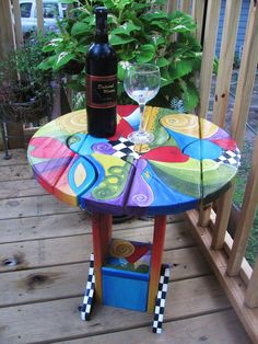 a colorful table with a wine glass and bottle on it next to a potted plant