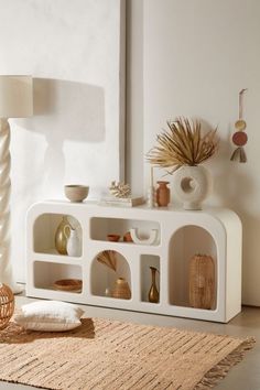 a living room with a white shelf and vases on the table next to it