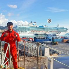 a man in an orange jumpsuit standing on a dock next to a cruise ship