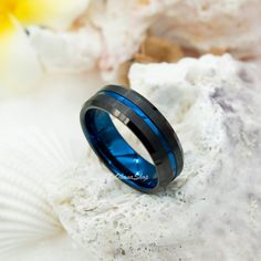 a black and blue wedding ring sitting on top of a piece of white rock next to a yellow flower