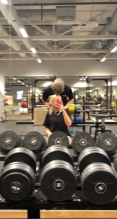 a man and woman standing next to each other in front of rows of dumbbells