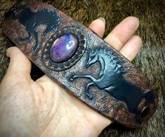 a hand holding a metal object with an animal design on it's side and purple stone in the middle