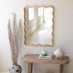 a wooden table with a vase and mirror on it next to a white painted wall