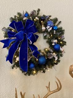 a christmas wreath with blue and white ornaments hanging on the wall next to deer antlers