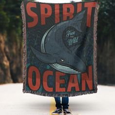 a person holding up a blanket with a whale on it that says spirit and ocean