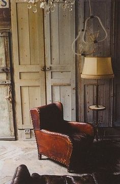 an old chair and footstools in a room with wooden paneling, chandelier and door