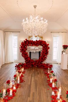 a room with candles, roses and a heart shaped wreath on the floor in front of a chandelier