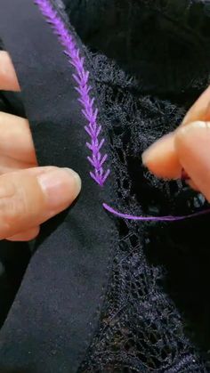 someone is stitching something with purple thread on the edge of a black piece of fabric