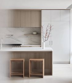 a white kitchen with two stools next to the counter top and an island in front of it