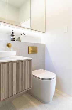 a white toilet sitting next to a sink in a bathroom under a mirror above it