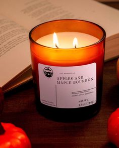 an apple and maple bourbon candle sitting next to apples on a table with a book