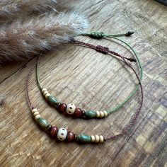 two necklaces on a wooden table with feathers in the background and a feather laying next to them