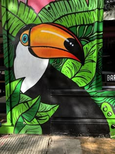 a painting of a toucan on the side of a building with green leaves