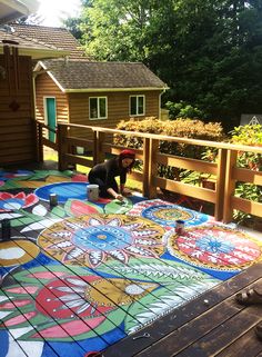 a person painting on the ground in front of a wooden fence with flowers and plants