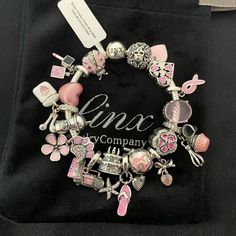 a pink and silver charm bracelet with various charms on it's side, sitting on a black velvet bag